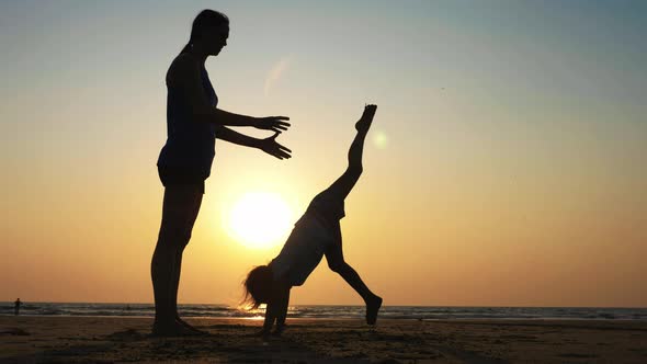 Silhouette of Mother with Daughter Doing Gymnastic on the Beach at Sunset