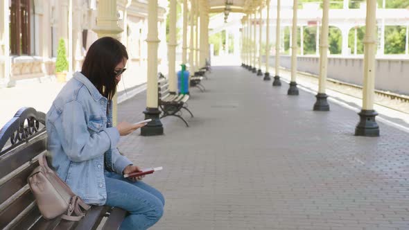 Young Woman with Phone in Hand Waiting on Railway Station for Train alt