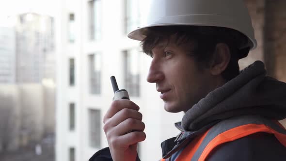 A Builder From a High-Rise Building Coordinates Work Using a Walkie-Talkie alt