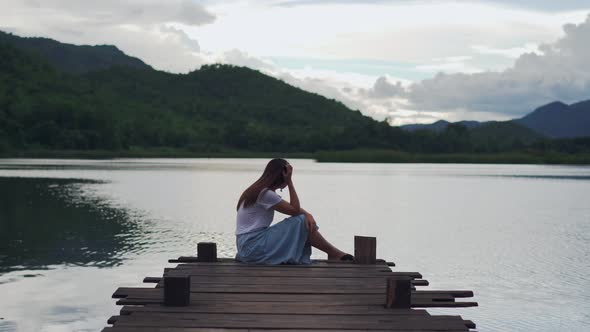 Depressed and stressed woman sitting on wooden pier and looking at the lake