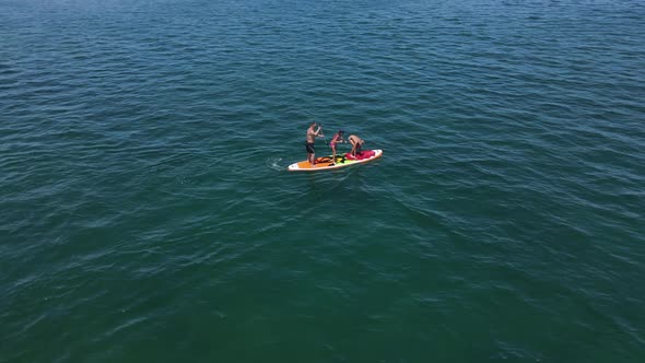 People on a paddle board, jumping into the water with splashes, aerial view.