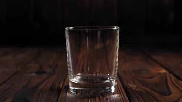 Closeup Ice Cubes Fall Into an Empty Glass on a Dark Wooden Background alt