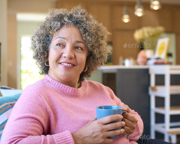 Mature Woman Sitting On Sofa At Home Relaxing With Hot Drink Stock ...