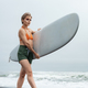 Female surfer clad in bikini top, shorts and barefoot, strides along sand beach, carrying surfboard - PhotoDune Item for Sale