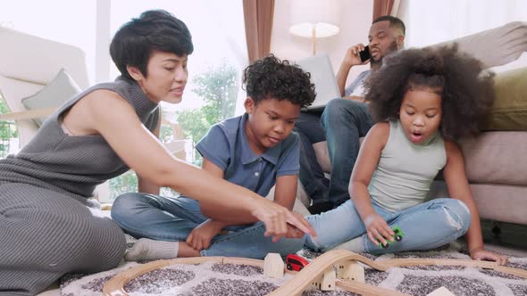 Mom plays with her kids on floor while her kid playing toy cars together at home