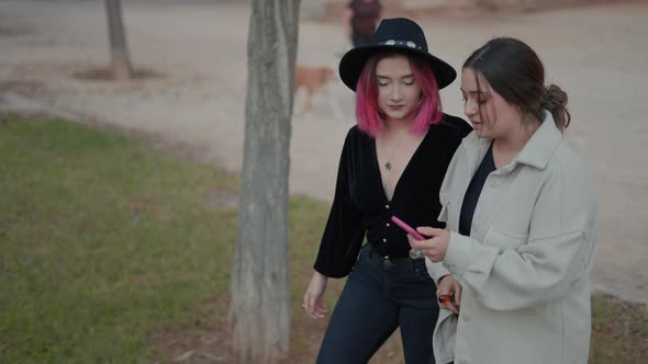 Young Women Walking Together While Looking to Cellphone Tracking Shot alt
