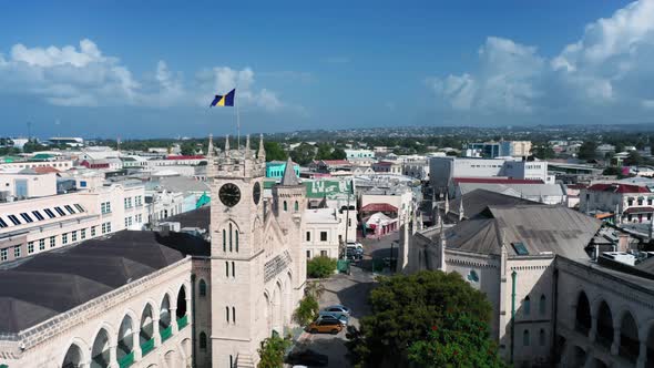 Drone moves over the roofs from Barbados Parliament building with barbadian flag in Bridgetown alt