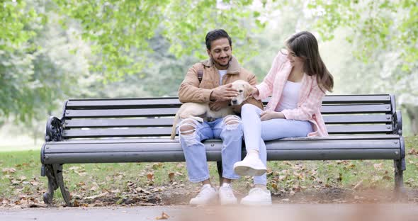 Happy couple sitting on park bench cuddling with dog