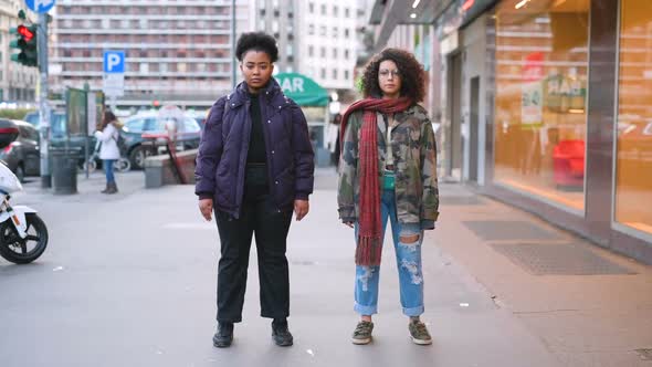 Time-lapse of two multiethnic women outdoor in the city standing looking camera serious alt