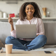 Smiling woman holding credit card while shopping online with laptop - PhotoDune Item for Sale
