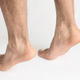 Two male feet standing on tiptoe showing tension in the Achilles tendon, with white background - PhotoDune Item for Sale