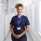 Portrait Of Smiling Female Nurse Wearing Uniform In Hospital Corridor With Security Lanyard - PhotoDune Item for Sale