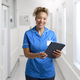 Portrait Of Smiling Female Nurse Wearing Uniform In Hospital Corridor With Digital Tablet - PhotoDune Item for Sale