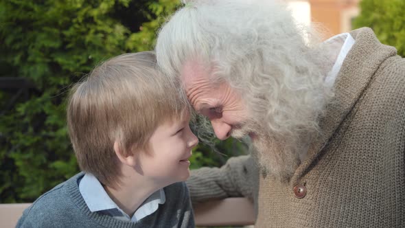 Close-up Side View of Joyful Grandfather and Grandson Rubbing Noses Outdoors. Portrait of Cheerful alt