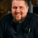 close-up in professional kitchen portrait of a chef in a black jacket in the kitchen happy smile - PhotoDune Item for Sale