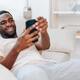 Happy African American Man Resting on Black Sofa Using Mobile Phone and Typing Message - PhotoDune Item for Sale