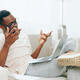 Smiling African American Man Working on Laptop at Home, Typing in Modern Living Room This image - PhotoDune Item for Sale
