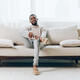 African American man sitting on a comfortable sofa in his modern home, looking sad and lost in - PhotoDune Item for Sale