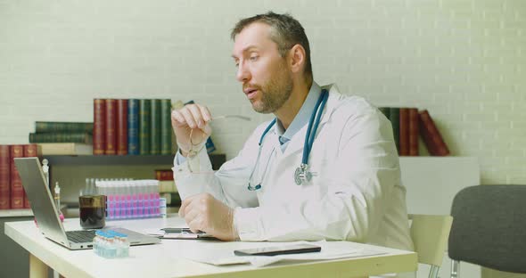 Middleaged Doctor Thinks Through a Research Report While Sitting in a Clinic Office alt