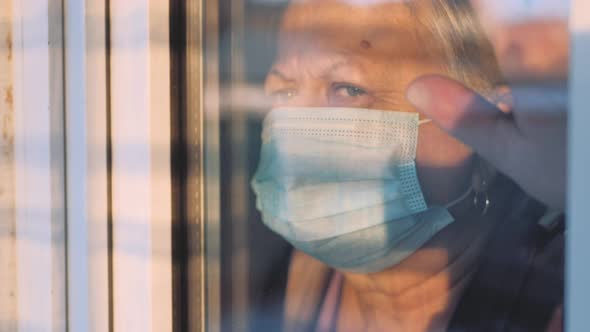 Elderly Woman at Window in Protecting Medical Mask on Selfisolation alt