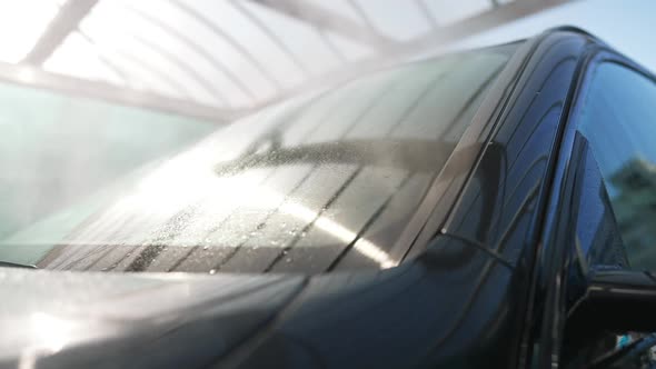 High Pressure Water Spraying on Car Windshield in Sunrays Shining Outdoors alt