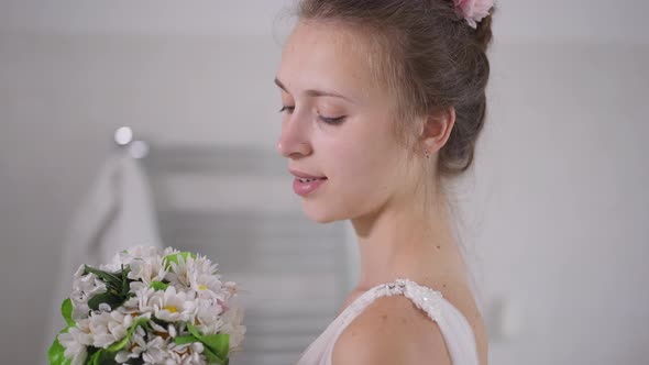 Side View Closeup Portrait of Happy Charming Young Caucasian Bride Admiring White Bridal Bouquet alt