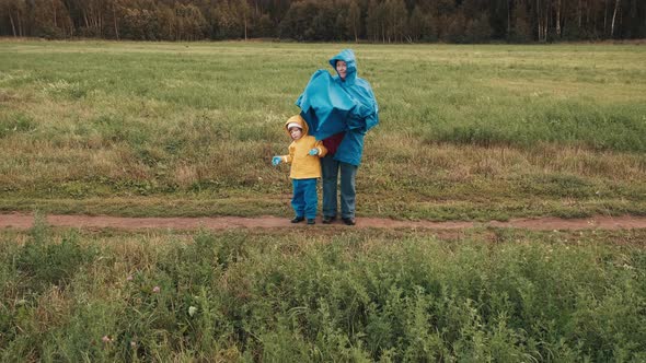 Mother Hides a Small Child From the Wind Under a Blue Raincoat