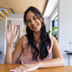 Young biracial woman waving, sitting at table indoors at home on a video call - PhotoDune Item for Sale
