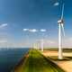 A row of elegant wind turbines stand tall next to a serene body of water, harnessing the power of - PhotoDune Item for Sale