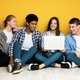Group of Four Teenagers Sharing Laptop While Sitting Against Yellow - PhotoDune Item for Sale