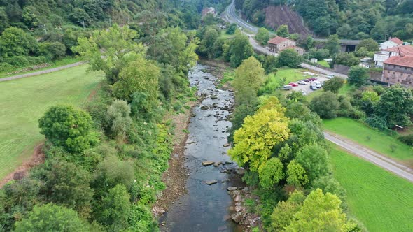 Flying over little river in rural hamlet surrounded by trees in Spain alt