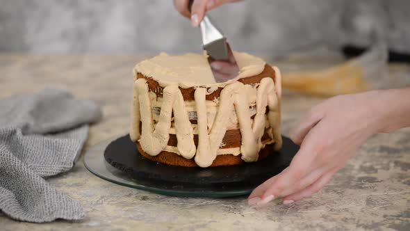 Girl Making a Cake in a Bakery. Baker Squeezes Cream Onto a Cake Layer. alt