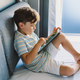 Young Boy Engrossed in playing tablet on a Cozy Couch During Afternoon Hours - PhotoDune Item for Sale