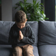 Young Boy Sitting on a Sofa With Hands Clasped in a Moment of praying - PhotoDune Item for Sale