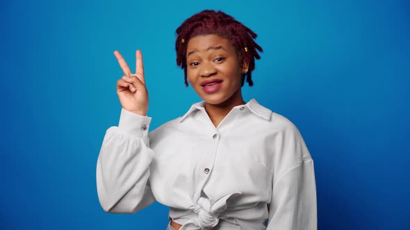 Joyful Happy Afro Woman Showing Victory Sign Against Blue Backgorund