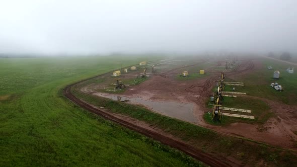 Aerial Flying Out View on Oil Pumps at Oilfield Cluster in a Foggy Field After Rain