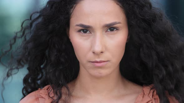 Sad Serious Hispanic Woman Outdoors Curly Brunette Girl in City Looks Down Looking at Camera Upset alt