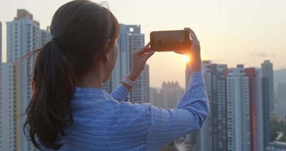 çWoman enjoy the view of the city and take picture on mobile phone under sunset view alt