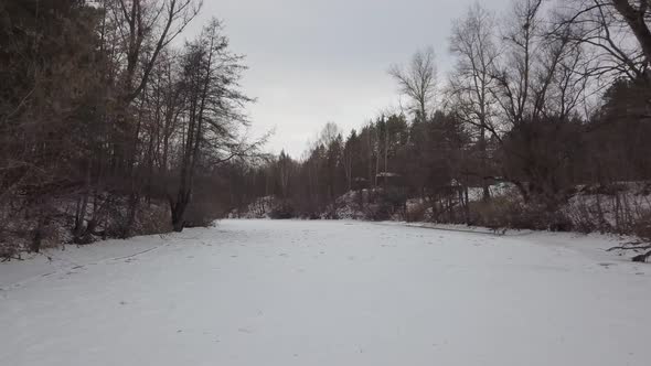 Extremely Low Flight of Drone Over Frozen River in Forest in Winter Day