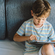 Young Boy Engrossed in playing tablet on a Cozy Couch During Afternoon Hours - PhotoDune Item for Sale
