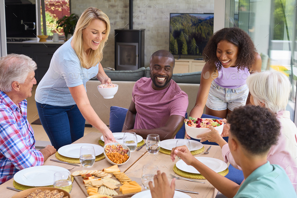 Three Generation Family Indoors Around Table At Home Serving And Eating ...