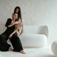 Hugs, on the white sofa. Two happy young female best friends are indoors - PhotoDune Item for Sale