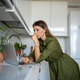 Thoughtful woman stands in front laptop table kitchen, focused on reading information from screen. - PhotoDune Item for Sale