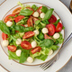 Salad with mozzarella, cherry tomatoes and green lettuce in a white round plate on the table - PhotoDune Item for Sale