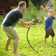 Funny little boy with his father playing with garden hose in sunny backyard. - PhotoDune Item for Sale