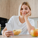 Young woman using cellphone, scrolling social media, doing online shopping while having breakfast. - PhotoDune Item for Sale