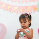 little latina brunette girl trying to open the embolture of a candy, happy birthday sign in spanish - PhotoDune Item for Sale