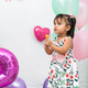 girl holding a candy in her hands while looking with intrigue, birthday balloons in the background - PhotoDune Item for Sale