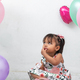 girl sitting on the ground surrounded by balloons, putting a hand to her mouth while looking up - PhotoDune Item for Sale