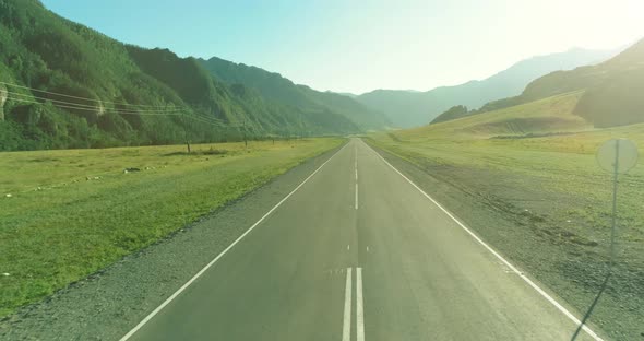 Aerial Low Air Flight Over Mountain Road and Meadow at Sunny Summer Morning. alt